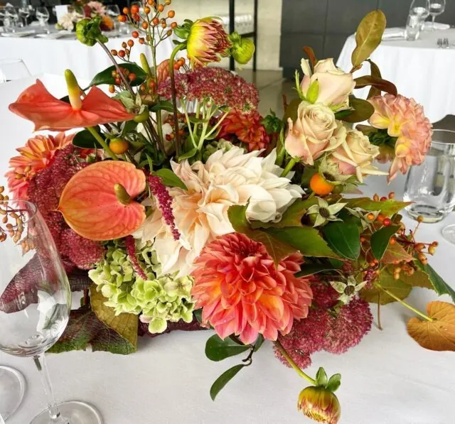An autumn centrepiece of coral dahlias, orange anthuriums and roses
