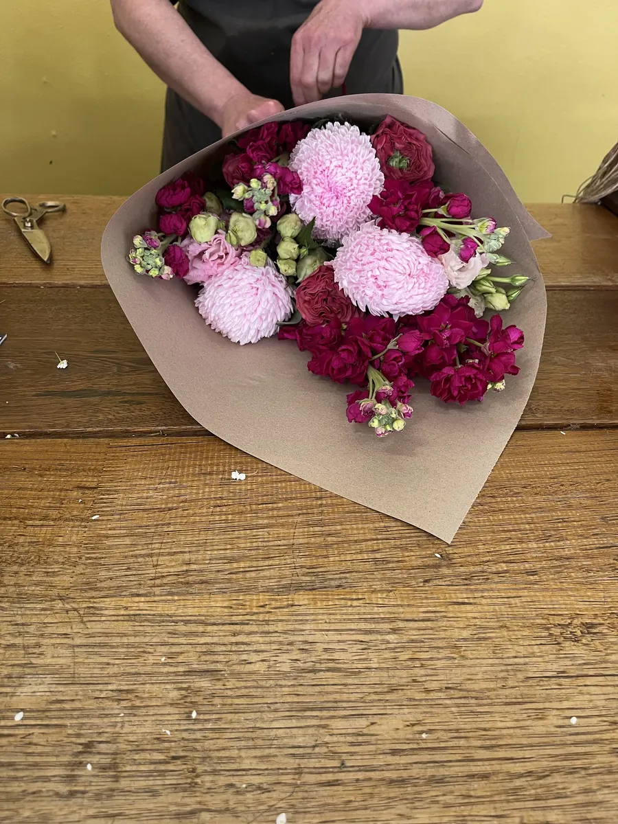 A bouquet of pink chrysanthemums and magenta stock being wrapped in kraft paper on the shop counter