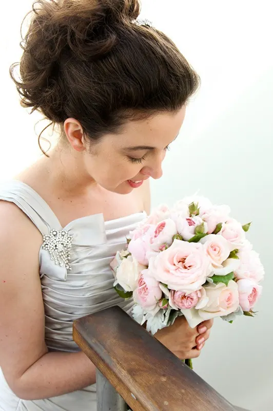 A bride holding a round posy of blush garden roses