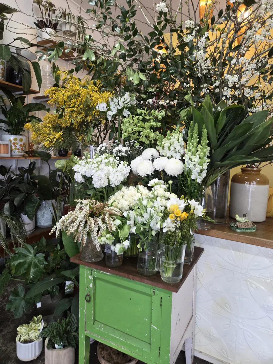 White flowers and greenery on the shop's green painted cabinet