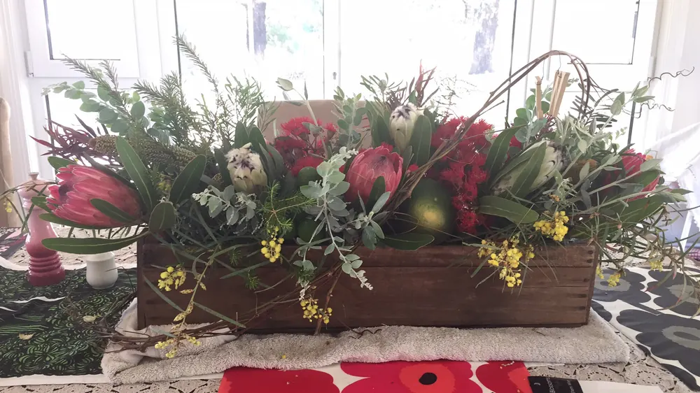 A long timber trough centrepiece of proteas, natives and trailing greenery