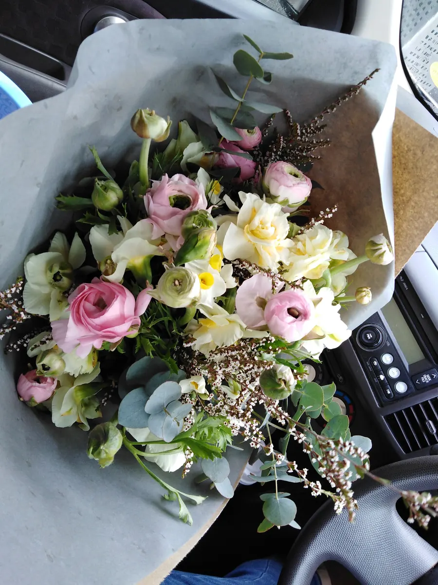 A wrapped posy of ranunculus, roses and eucalyptus on the passenger seat, ready for delivery